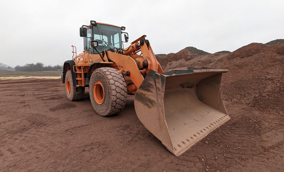 Een oranje wiellader met een volle bak naast grindhopen