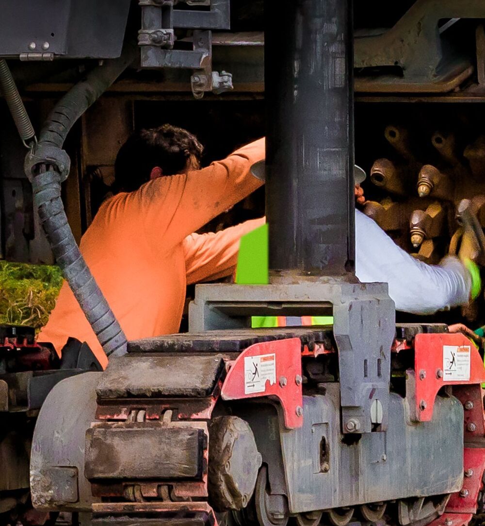 Twee technici werken onder een machine met rupsen